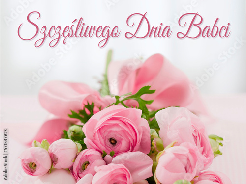 kartka lub baner z życzeniami szczęśliwego dnia babci w kolorze różowym na szarym tle z efektem bokeh i poniżej bukietem różowych kwiatów