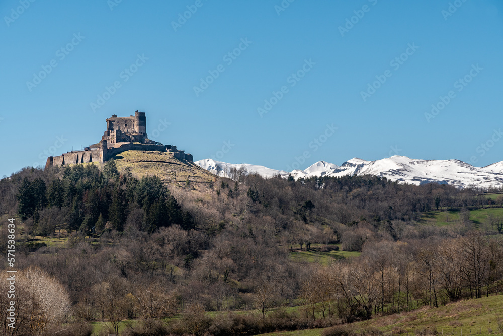 château de Murol dans le puy de dôme, sur son promontoire avec en arrière plan la chaine de montagne du Sancy enneigée par une belle journée de début de printemps