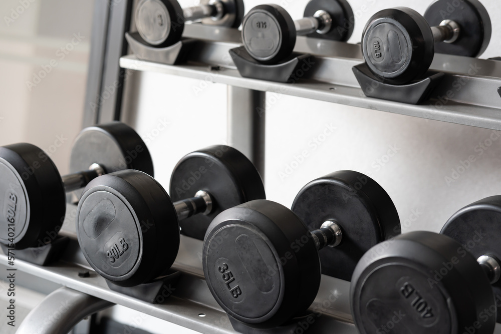 Stand with dumbbells. Sports and fitness room. Weight Training Equipment. Black dumbbell set, many dumbbells on rack in sport fitness center Stand with dumbbells. Sports and fitness room. Weight Training Equipment. Black dumbbell set, many dumbbells on rack in sport fitness center