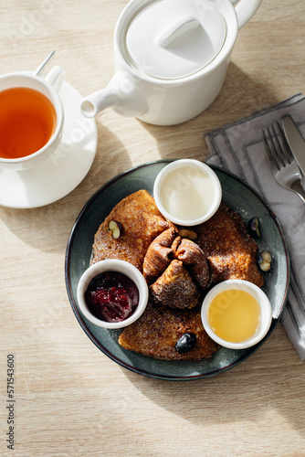 Delicious thin pancakes with jam, honey and sour cream and cup of tea on light wooden table. Morning breakfast concept. Top view.