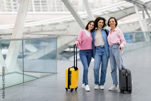 Portrait Of Three Happy Female Friends Posing At Airport Terminal