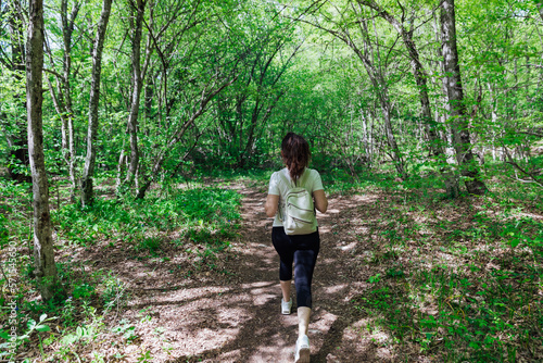 a woman with a backpack walks through the forest among the green trees hiking journey