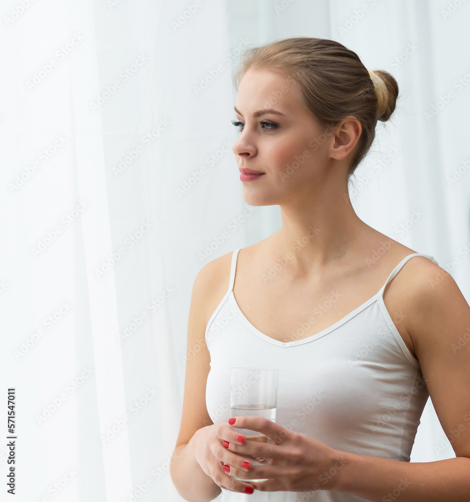 Young woman in white underwear is standing in front of the window and looking into it. Girl at home in the living room. Young woman in white underwear is standing in front of the window and looking into it. Girl at home in the living room.