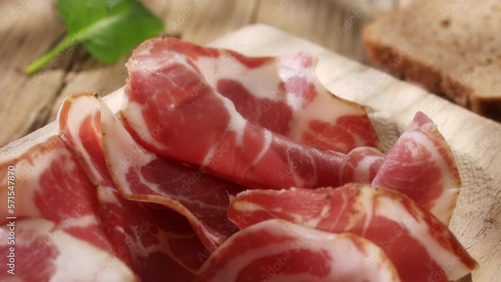meat delicacy close-up with green leaves on a wooden background. dry-cured pork on a tray. meat with a layer of fat under sunlight. traditional snack in rustic style. meat delicacy close-up with green leaves on a wooden background. dry-cured pork on a tray. meat with a layer of fat under sunlight. traditional snack in rustic style.