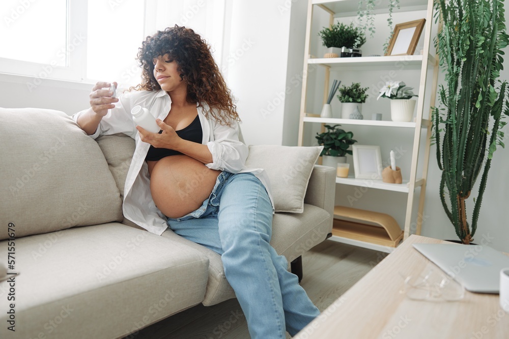 Pregnant woman smile blogger takes vitamins sitting on the couch at home freelancer in the last month of pregnancy lifestyle before childbirth Pregnant woman smile blogger takes vitamins sitting on the couch at home freelancer in the last month of pregnancy lifestyle before childbirth