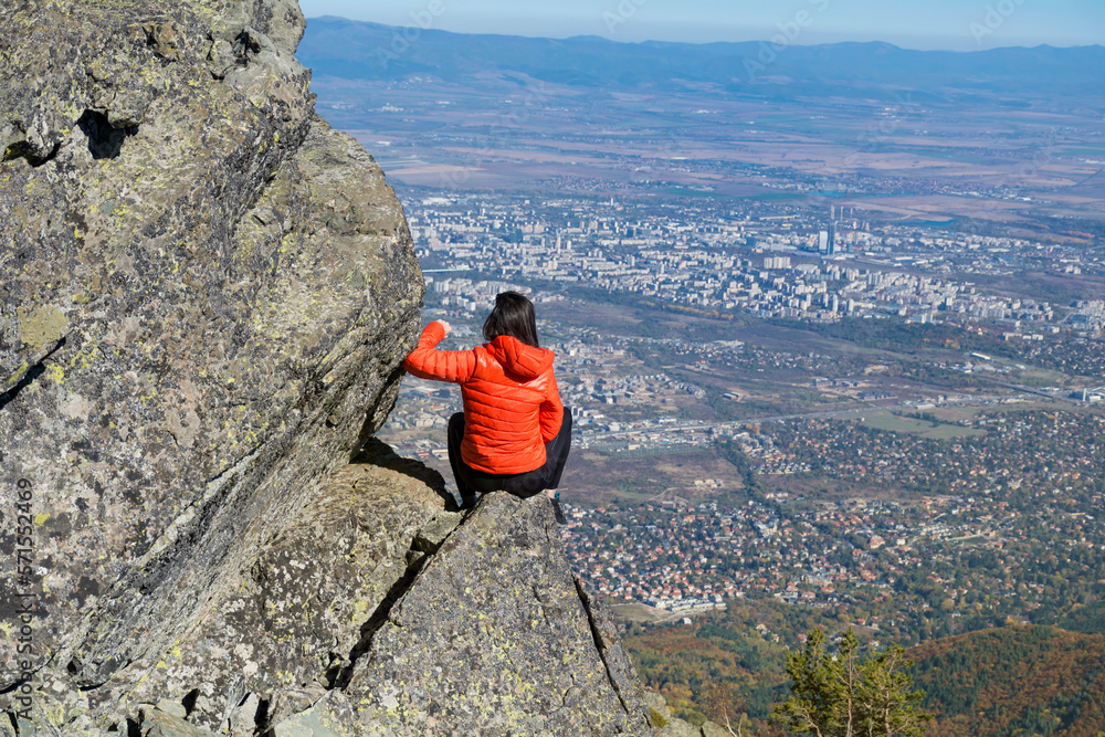 Obraz premium Woman sitting on a rocks high in the autumn mountain above the city of Sofia. Vitosha mountain, ,Bulgaria