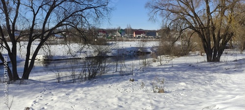 European panoramic winter landscape with bare trees on snow on river coast at Sunny winter day