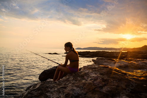  Child girl have fun on the sea rocky shoreline fishing at sunset light. Summer travel holiday. Beautiful summer scene. 