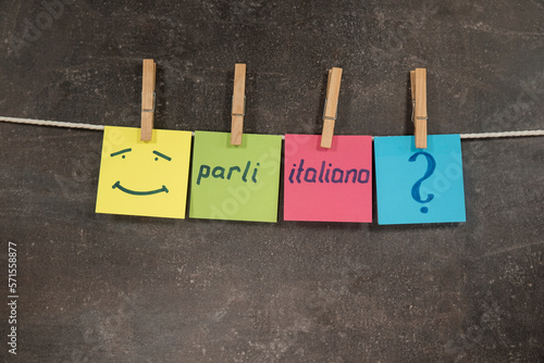 Napis Parli italiano na kolorowych karteczkach wiszących na ciemnym tle photo