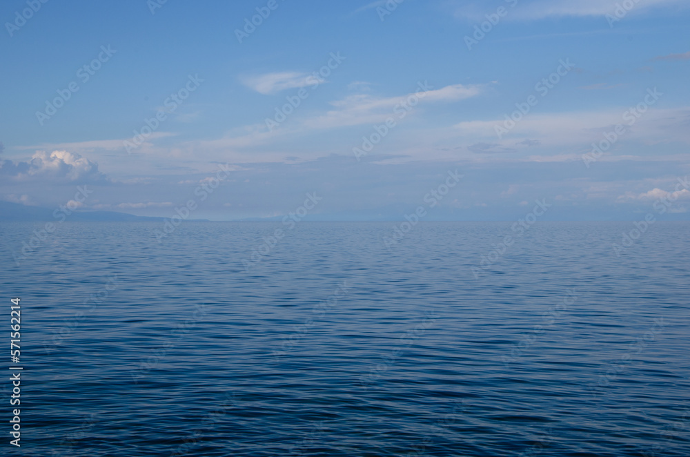 The calm and clean surface of the lake merges with the blue sky on the horizon. A sunny summer day.