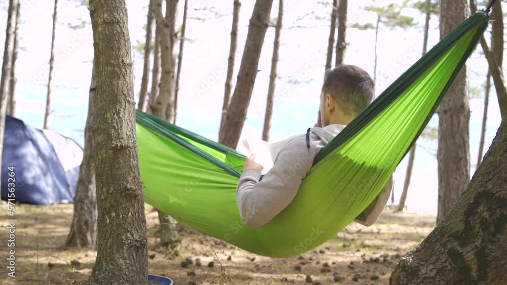 European young man reading outside in the summer near trees and tents near the Black Sea European young man reading outside in the summer near trees and tents near the Black Sea