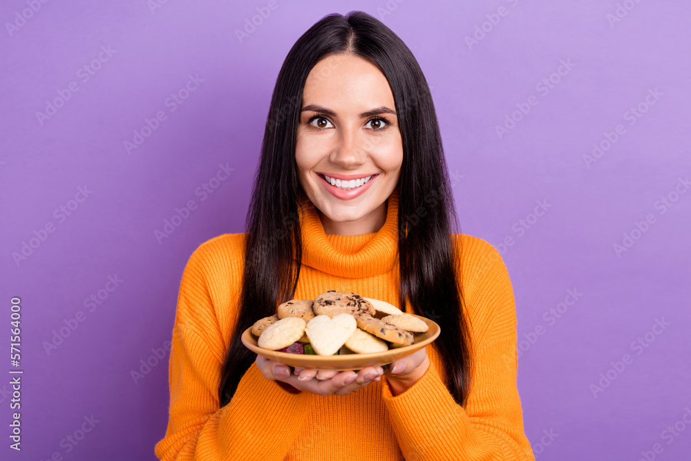 Portrait photo of pretty cooker woman wear orange turtleneck hold cookies enjoy bakery fresh tasty food yummy isolated on purple color background Portrait photo of pretty cooker woman wear orange turtleneck hold cookies enjoy bakery fresh tasty food yummy isolated on purple color background