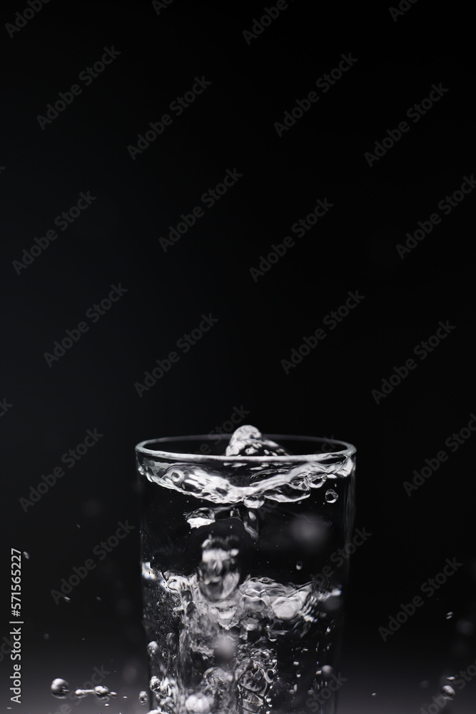 natural mineral clean healthy water in a transparent glass and drops of water splash out of it on a dark background. for banners labels splash screens postcards advertising signage