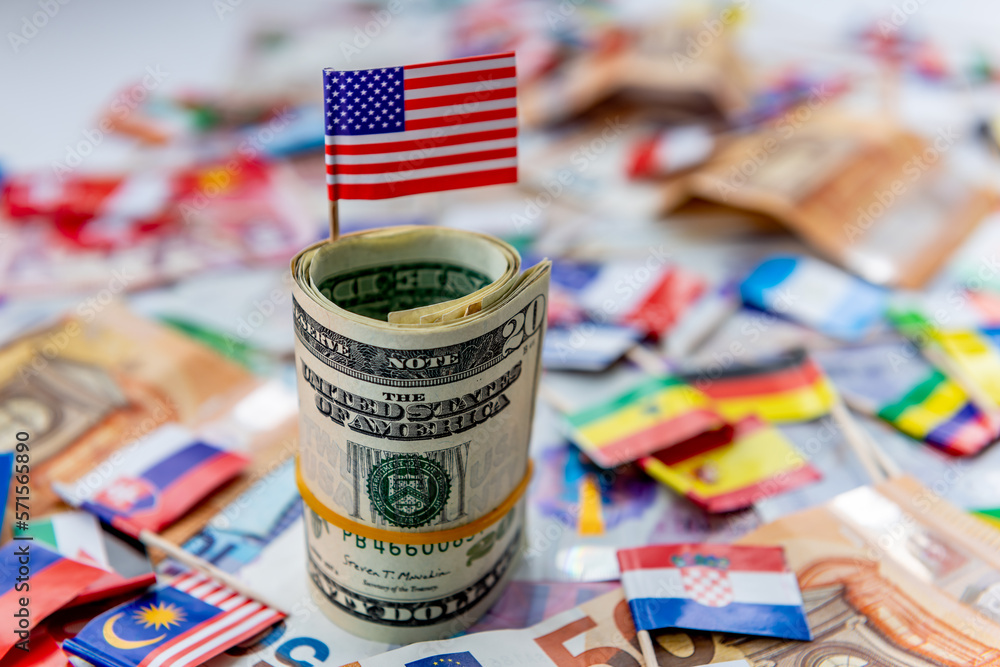 A roll of US dollars with the American flag on top of a other currencies and country flags. Dollar hegemony concept. - obrazy, fototapety, plakaty 