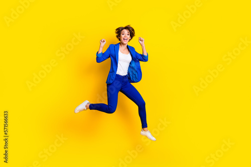 Full length photo of shiny lucky woman wear blue jacket rising fists screaming jumping high isolated yellow color background © deagreez