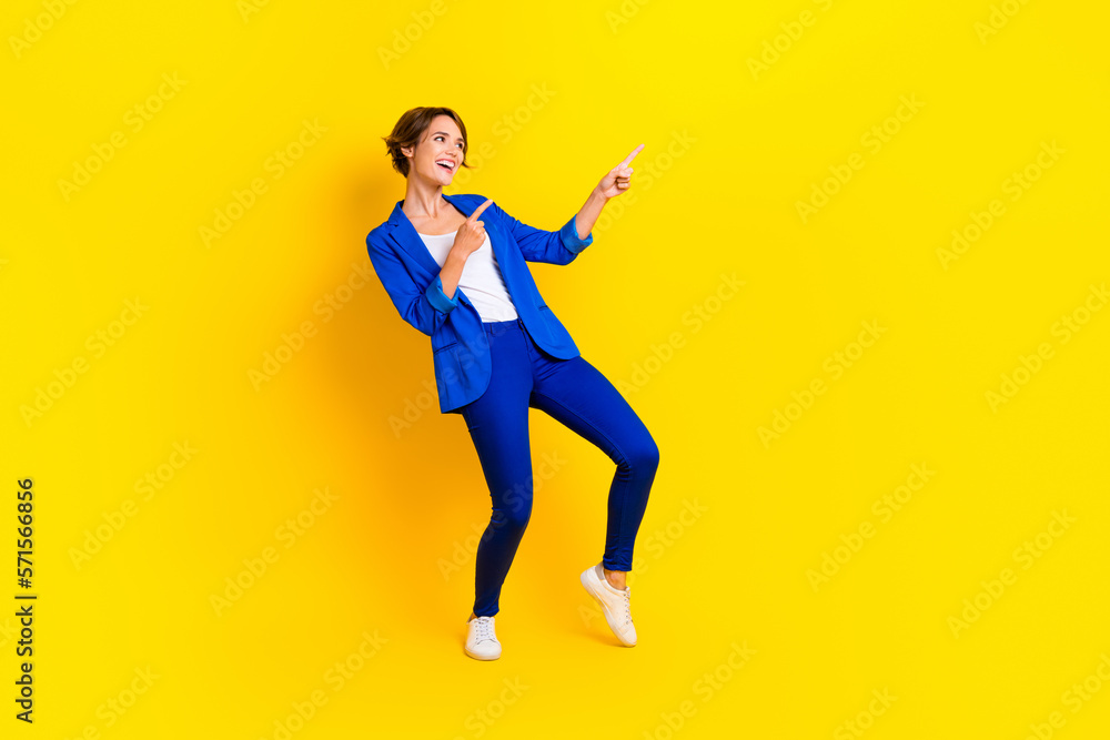 Full length photo of excited pretty woman wear blue jacket looking pointing two fingers empty space isolated yellow color background