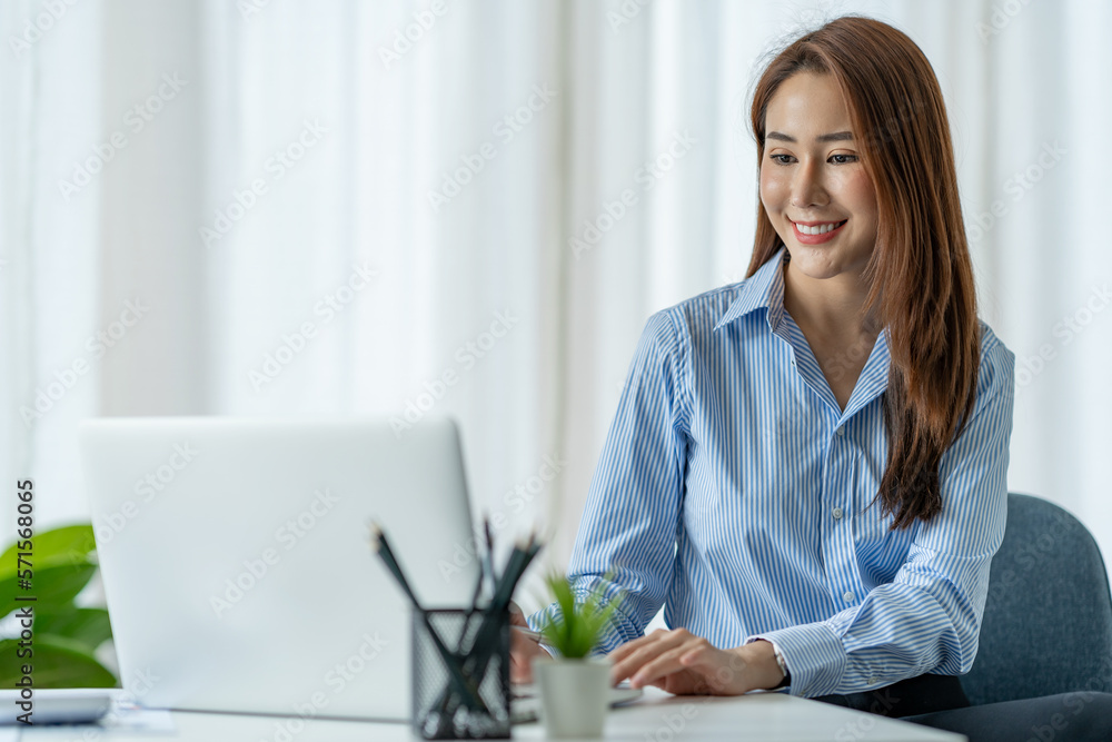 Beautiful Asian businesswoman sitting at work saving data Happy checking financial details on laptop computer in the office. Beautiful Asian businesswoman sitting at work saving data Happy checking financial details on laptop computer in the office.