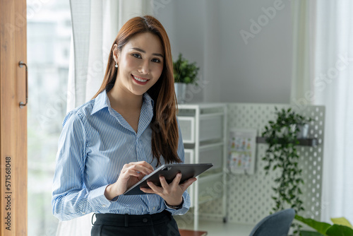 A pretty smiling Asian businesswoman holding a tablet to look at financial details, and online delivery orders in the office happily.