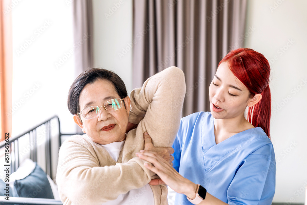 Nurse caregiver wearing scrubs exercises with a senior Asian woman to relieve a frozen shoulder of the senior patient with physiotherapy treatment. Home health care and nursing home concept. Nurse caregiver wearing scrubs exercises with a senior Asian woman to relieve a frozen shoulder of the senior patient with physiotherapy treatment. Home health care and nursing home concept.