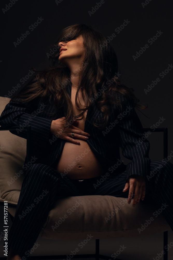 Beautiful pregnant girl at the studio. A pregnant girl in a man's suit.Stunning pregnant woman - maternity photography of a beautiful young expecting mother to be on a black background, studio photogr Beautiful pregnant girl at the studio. A pregnant girl in a man's suit.Stunning pregnant woman - maternity photography of a beautiful young expecting mother to be on a black background, studio photogr