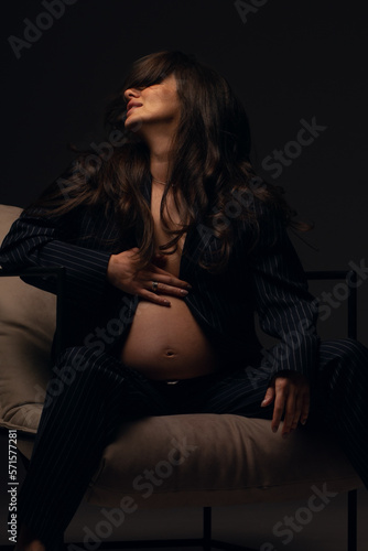 Beautiful pregnant girl at the studio. A pregnant girl in a man's suit.Stunning pregnant woman - maternity photography of a beautiful young expecting mother to be on a black background, studio photogr © pha88