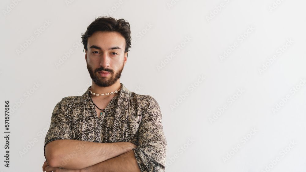 Panoramic photo of a young queer gay latin man looking at camera with his arms crossed on a white background. Copy space. Panoramic photo of a young queer gay latin man looking at camera with his arms crossed on a white background. Copy space.