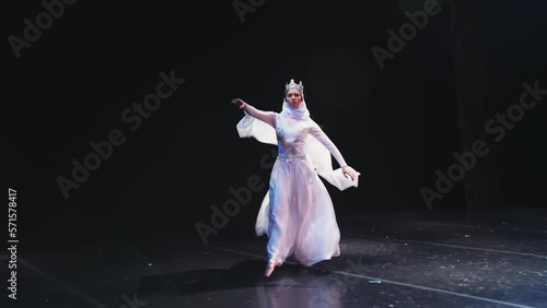 The ballerina goes on stage. A ballet dancer in a beautiful white robe dances on a black background. Raymonda Variation. photo