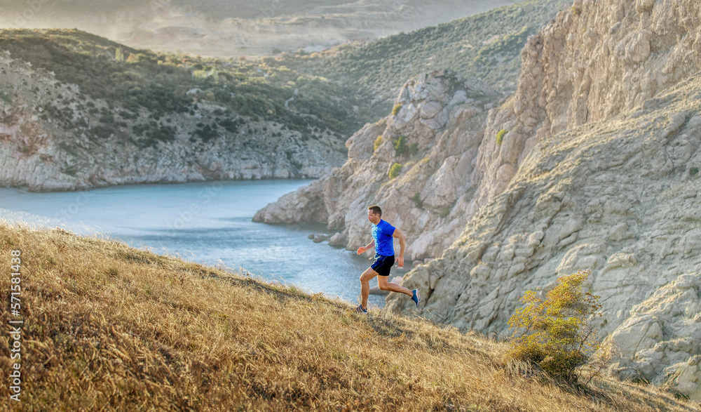man athlete running uphill background of sea bay and rocks in sunset
