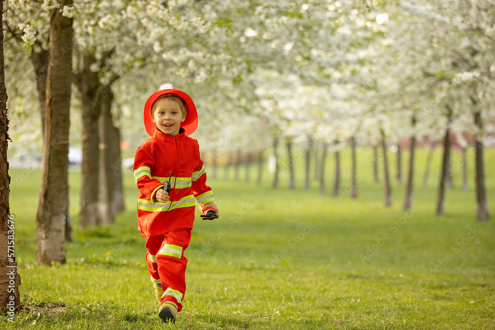 Little toddler child with fireman costume in park, pretending to be real fireman, playing Little toddler child with fireman costume in park, pretending to be real fireman, playing