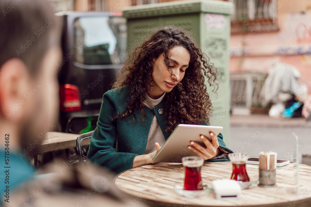Fototapeta premium Beautiful curly businesswoman using digital tablet outdoors in cafe