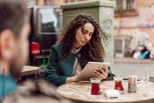 Beautiful curly businesswoman using digital tablet outdoors in cafe