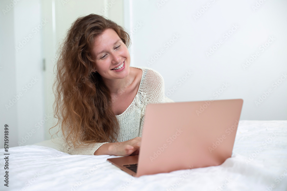 Happy joyful woman is using laptop computer at home on bed in bedroom and smiling Happy joyful woman is using laptop computer at home on bed in bedroom and smiling