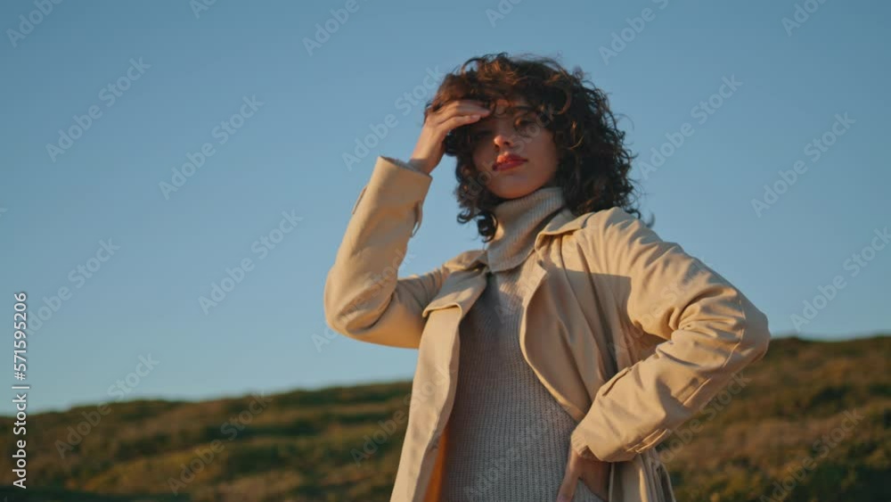 Casual girl posing evening sunlight at seaside. Pretty smiling woman touch hair Casual girl posing evening sunlight at seaside. Pretty smiling woman touch hair