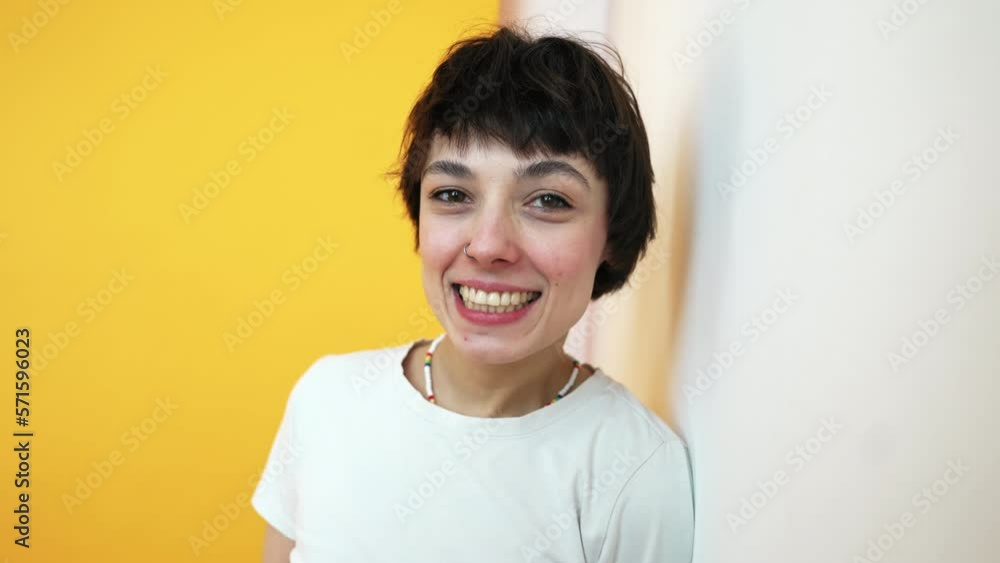 Happy short-haired girl leaning back on white wall and looking at camera. Copy space studio shot on orange background. High quality 4k footage Happy short-haired girl leaning back on white wall and looking at camera. Copy space studio shot on orange background. High quality 4k footage
