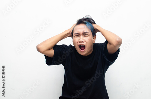 asian man with peek a boo hair screaming madly and angrily. asian man looks depressed and messed up. Irritated man bites lips and scratches head. stressed over work concept. asian man looks furious 