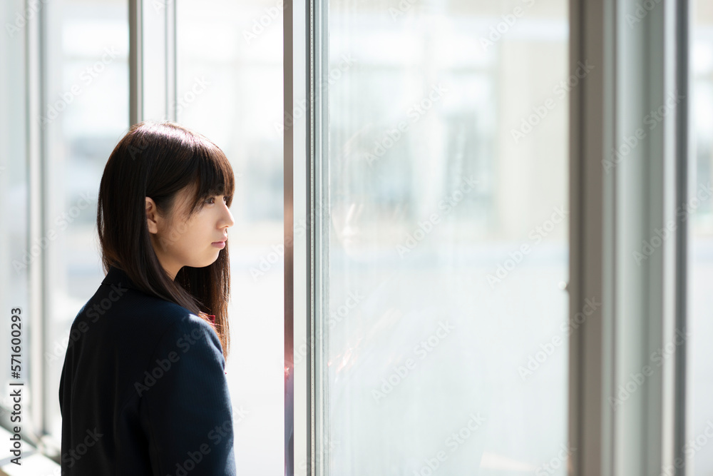 窓際で遠くを眺める女子学生 窓際で遠くを眺める女子学生