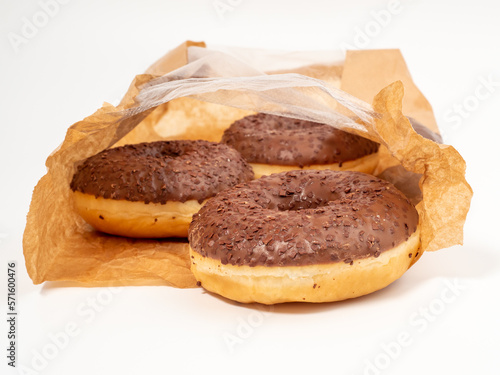 Chocolate donut with chocolate chips in a paper bag on a white background. close-up.