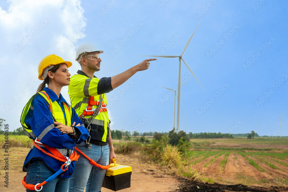 Male and female engineers wearing reflective safety jackets walk to work together to repair wind turbines, bringing wind energy to generate electricity at the wind farm.