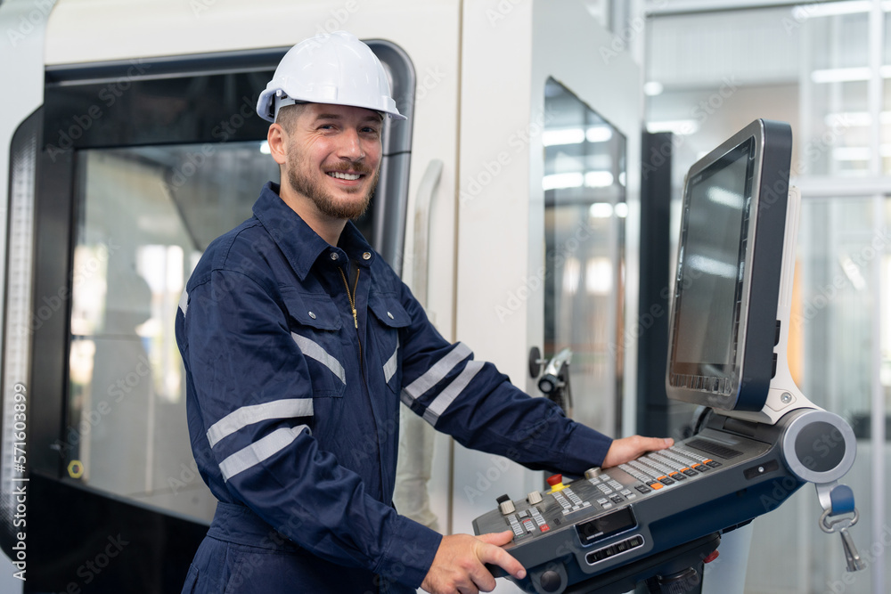 Male engineer operating cnc machine in control panel at factory. Smiling man technician in uniform and helmet safety working at workshop heavy metal industrial Male engineer operating cnc machine in control panel at factory. Smiling man technician in uniform and helmet safety working at workshop heavy metal industrial