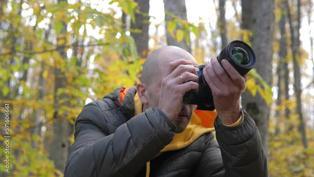 Portrait of the interested photographer looking up at the autumn forest landscape, leaning into his camera, pressing shutter release and taking some photos. Active tourism and hobby concept. Portrait of the interested photographer looking up at the autumn forest landscape, leaning into his camera, pressing shutter release and taking some photos. Active tourism and hobby concept.