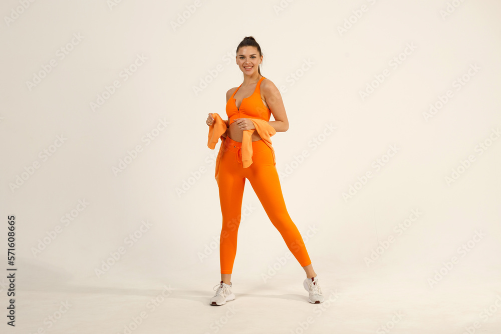 Young positive smiling woman in orange fitness sport outfit cloth studio isolated shot.
