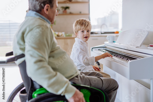 Little boy playing on the piano with his grandfather on wheelchair.