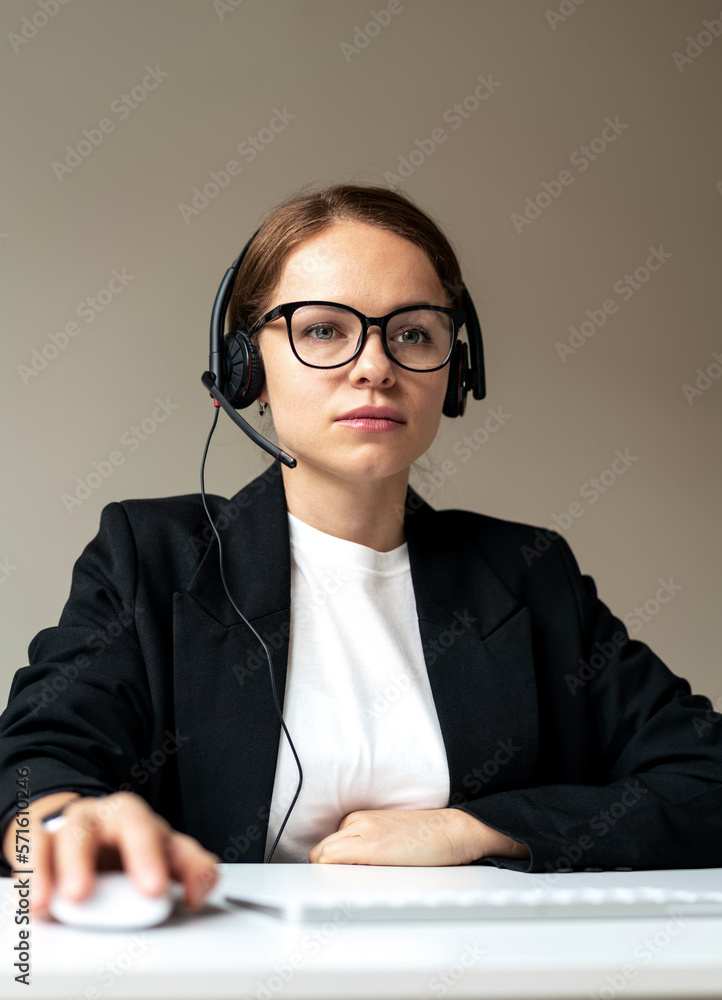 Shot of serious woman office worker in glasses and headset sitting at desk working at computer. Shot of serious woman office worker in glasses and headset sitting at desk working at computer.