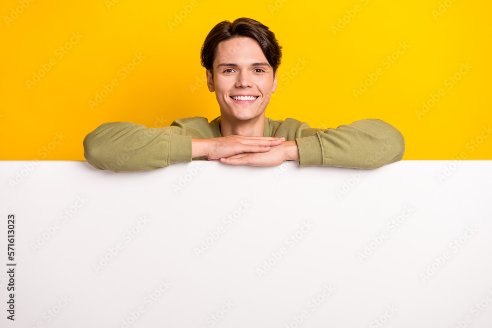 Photo of cheerful nice man wear stylish clothes stand behind white wall presenting empty space isolated on yellow color background Photo of cheerful nice man wear stylish clothes stand behind white wall presenting empty space isolated on yellow color background