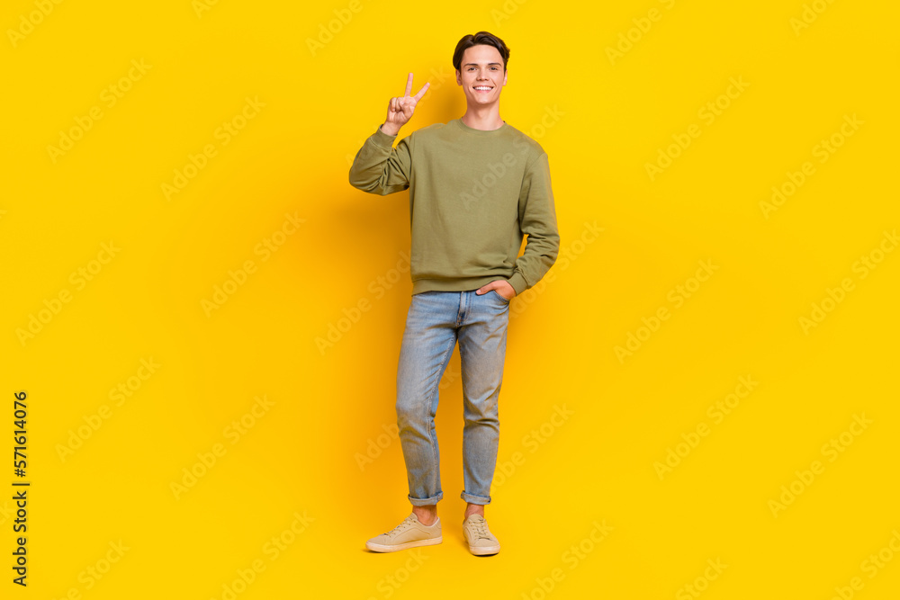 Fototapeta premium Full body portrait of cheerful glad young man hand fingers demonstrate v-sign isolated on yellow color background