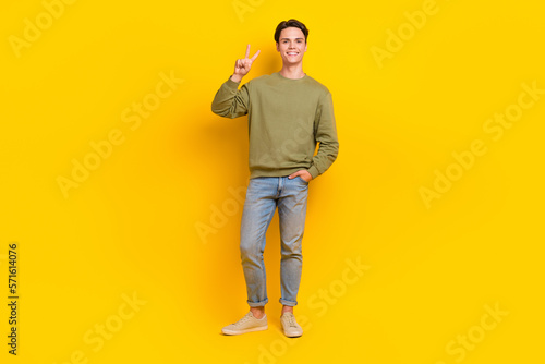 Full body portrait of cheerful glad young man hand fingers demonstrate v-sign isolated on yellow color background