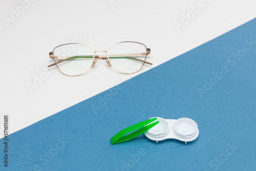 Container with contact lenses, glasses and tweezers on color background