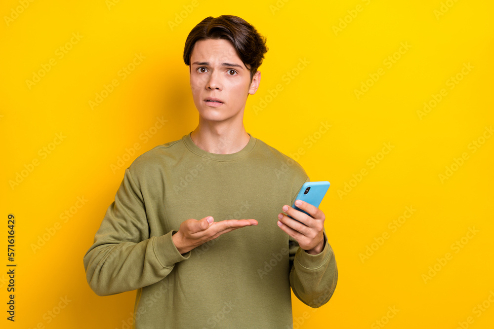 Photo of upset stressed man demonstrate telephone uncertain quality device stand near empty space isolated on yellow color background Photo of upset stressed man demonstrate telephone uncertain quality device stand near empty space isolated on yellow color background