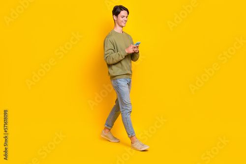 Full body profile portrait of positive person use telephone typing write walking isolated on yellow color background