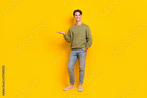 Full length photo of cheerful man wear fashionable clothes arm presenting empty space low prices offer isolated on yellow color background